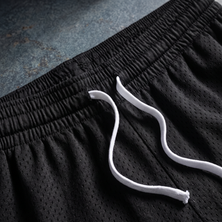 Close-up of the elasticated waistband and flat white drawstring on the black Nomenclature mesh shorts