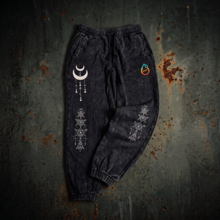 Existential 420 GSM black snow wash heavyweight joggers laid flat on dark weathered steel, showing the drawstring elastic waistband, side pockets, ribbed ankle cuffs, the cream crescent moon and sacred geometry prints down the leg and the pH flame logo on the hip.