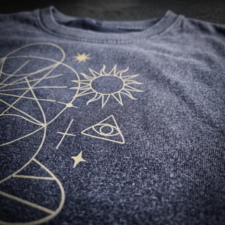 Macro of the pale gold screen printed sun, all-seeing eye triangle and stars on the Dimensional Drift tank top, raking light showing the 275 GSM cotton knit grain and the snow wash mottling.