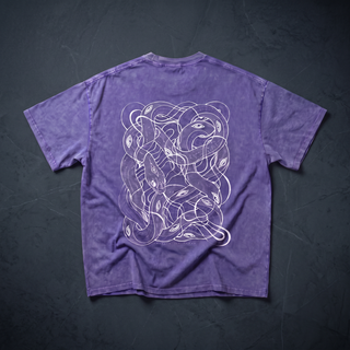 Back of the Embrace The Chaos Patakota collab tee in Purple Haze snow wash, crumpled into a styled flat lay on dark charcoal slate, printed in white line art with a dense tangle of intertwined serpents and eyes.