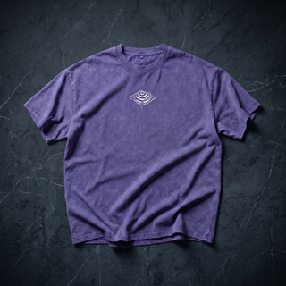 Front of the Embrace The Chaos Patakota collab tee in Purple Haze snow wash, crumpled into a styled flat lay on dark charcoal slate, with the small white eye-and-saucer graphic printed at the chest.