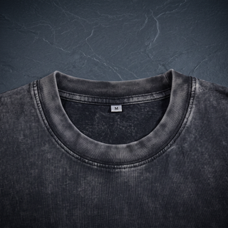 Close-up of the ribbed crew neckline and interior size label on the 250 GSM black snow wash heavyweight tee, shot on dark charcoal slate.