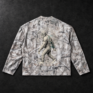 Studio flat lay of the PsySquatch tree camo waffle knit long sleeve on charcoal concrete, back view, the sasquatch resolving out of the all over snow tree camo with a Flower of Life mandala ghosted into the branches, teal mycelium on the shoulder and mushrooms at the feet