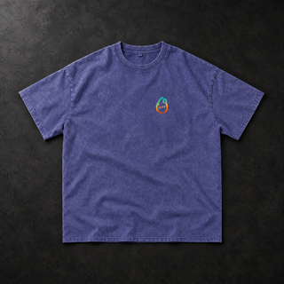 Studio flat lay of the PsySquatch snow wash oversized tee in Purple Haze on charcoal concrete, front view, soft directional light across the dusty violet mineral wash, relaxed drop shoulder sleeves and the small cyan to orange drop mark on the left chest