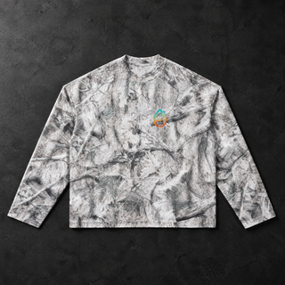 Studio flat lay of the PsySquatch tree camo waffle knit long sleeve on charcoal concrete, front view, soft directional light across the high key snow tree camo of branches and pine needles, ribbed crew collar, visible waffle texture and the small cyan to orange drop mark on the chest
