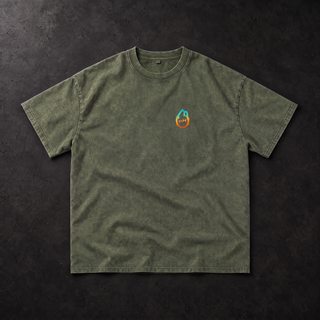 Studio flat lay of the PsySquatch snow wash oversized tee in Bean Green on charcoal concrete, front view, soft directional light across the moss green mineral wash, relaxed drop shoulder sleeves and the small cyan to orange drop mark on the left chest