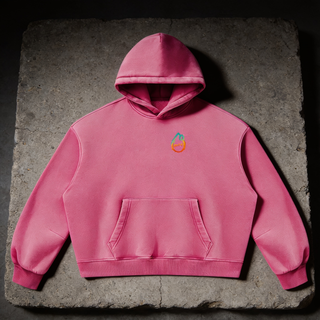 Studio flat lay of the Rose Red PsySquatch vintage wash boxy fleece hoodie on weathered charcoal concrete, front view, showing the 390 GSM washed fleece, kangaroo pocket, ribbed cuffs and hem, and the small cyan to orange drop mark on the chest
