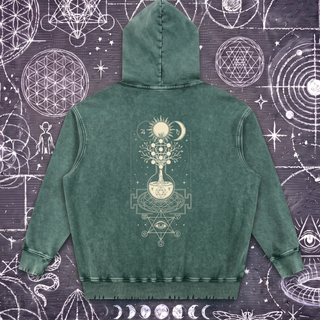 Blackish green Celestial Synthesis snow wash hand-frayed heavyweight hoodie laid flat on wet chalk-covered pavement, showing the cream alchemical tree of life, flask and all-seeing eye print on the back.