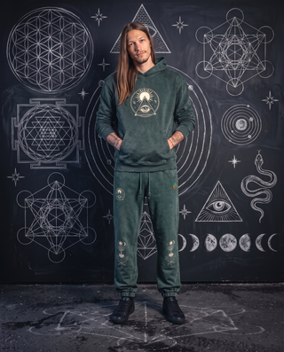 Model 6'0" and 165 lb wearing the blackish green Celestial Synthesis snow wash joggers with the matching hand-frayed hoodie in front of a chalkboard wall of white chalk sacred geometry.