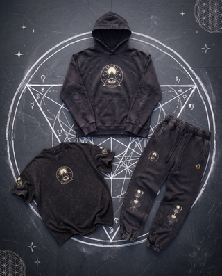 Black Celestial Synthesis 3-piece set, tee, hoodie and joggers arranged around a hand-drawn white chalk circle with sacred geometry on dark slate.
