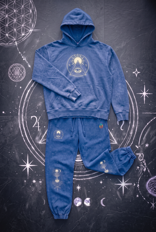 Royal blue Celestial Synthesis hoodie and joggers set laid out as one outfit on dark slate with white chalk sacred geometry, cream sun and all-seeing eye emblem on the hoodie chest and jogger thigh, tree of life on both knees.