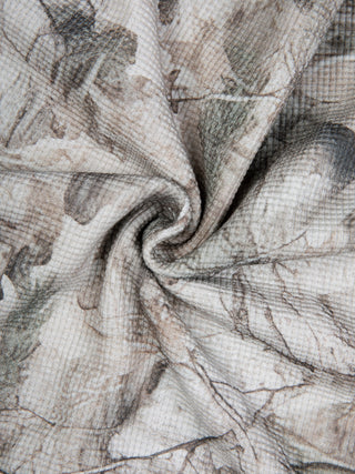 Close up of the tree camo waffle knit fabric twisted to show the raised waffle cells under the all over snow camo print of branches and leaves, 260 GSM cotton and polyester blend