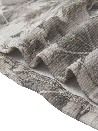 Detail of the straight hem and side seam stitching on the PsySquatch tree camo waffle long sleeve, showing the print running unbroken over the seam