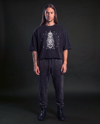 Model wearing the Oracle mineral wash raw-hem DJ cut heavyweight tee in Black, front view, showing the cropped boxy cut and the white deity totem artwork on the chest.
