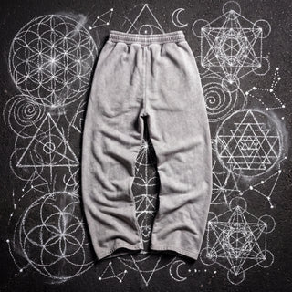 Back of the Paradigm snow washed baggy heavyweight sweatpants in light gray, laid flat on dark asphalt covered in white chalk sacred geometry, showing the plain back, elastic waistband and wide straight legs.