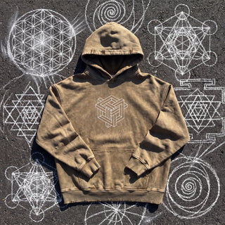 Front of the Paradigm snow wash hand-frayed heavyweight hoodie in brown, laid flat on dark asphalt covered in white chalk sacred geometry, with a white impossible-geometry cube knot printed on the chest, a kangaroo pocket and a hand-frayed hood, cuffs and hem.