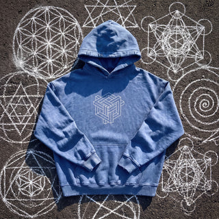 Front of the Paradigm snow wash hand-frayed heavyweight hoodie in royal blue, laid flat on dark asphalt covered in white chalk sacred geometry, with a white impossible-geometry cube knot printed on the chest, a kangaroo pocket and a hand-frayed hood, cuffs and hem.