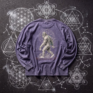 Back of the PsySquatch acid wash oversized long sleeve tee in Purple Haze, styled on dark asphalt covered in white chalk sacred geometry, showing a bigfoot walking in front of a flower of life halo.