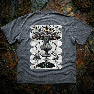 Gray Sacred Shroom fluffy vintage oversized tee, back view on mossy rock, printed in black and cream with an eyed mushroom cap, rising sun, chalice and spotted mushrooms.