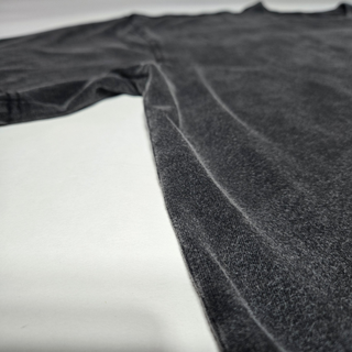 Low-angle flat lay of acid-washed charcoal Spaced Out tee showing body and sleeve on white surface